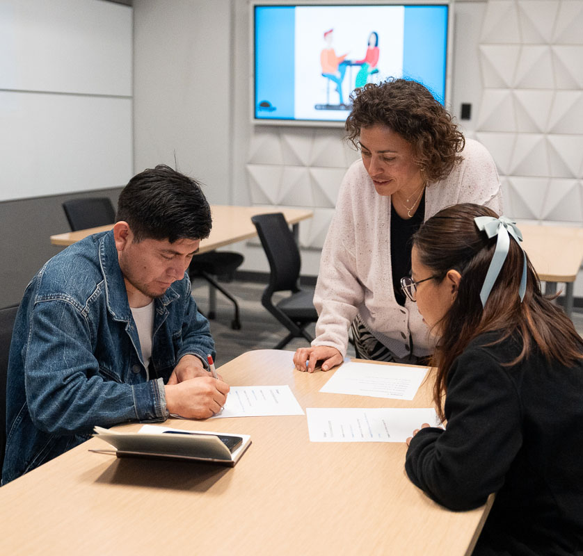 A woman teaches an English as a second language class to a small group of students.