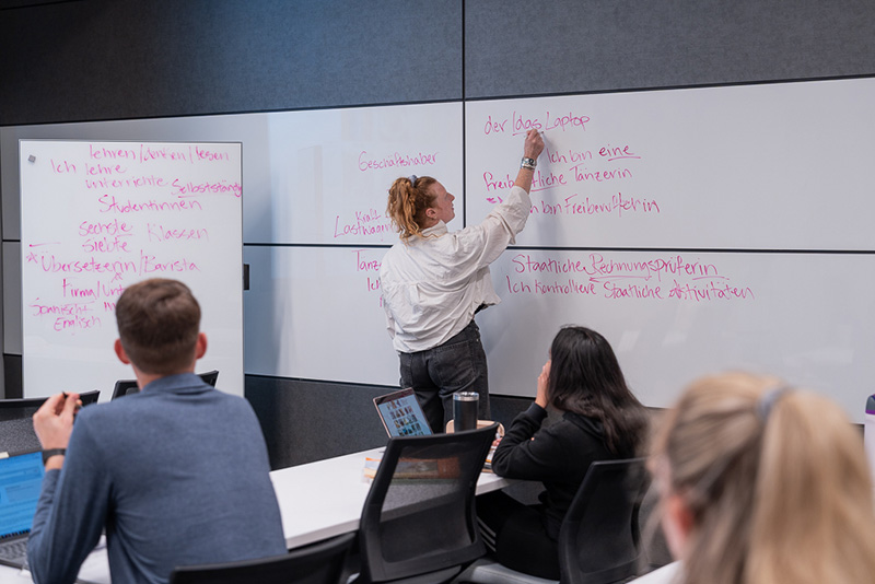 A woman writes in German on a white board in a classroom.
