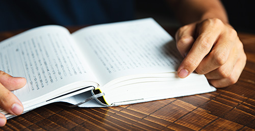 A person holds open a Japanese book on a desk.