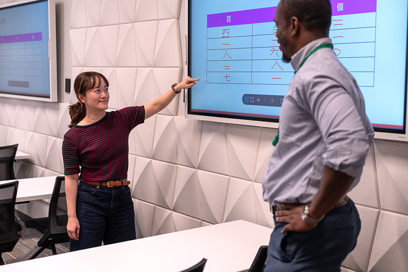 An instructor teaches a student Japanese kanji characters on a whiteboard screen.
