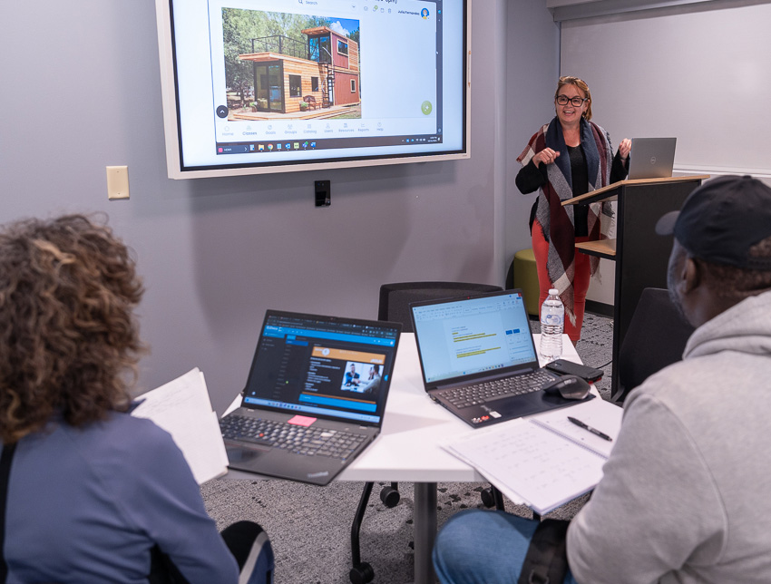 A woman stands behind a podium teaching Spanish in a small classroom.