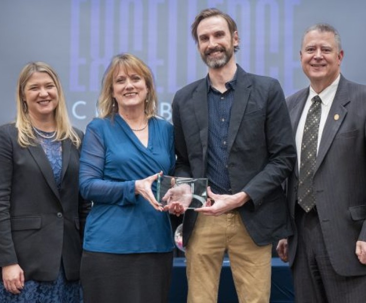 Four people standing with two holding an award 