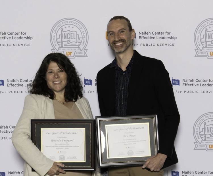 A man and a woman pose with framed certificates