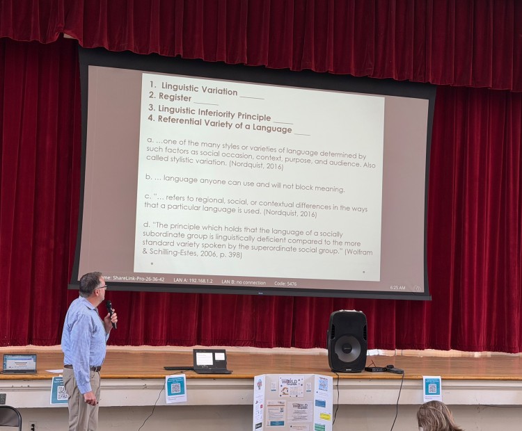 Man with microphone standing in front of a presentation screen with a slide showing