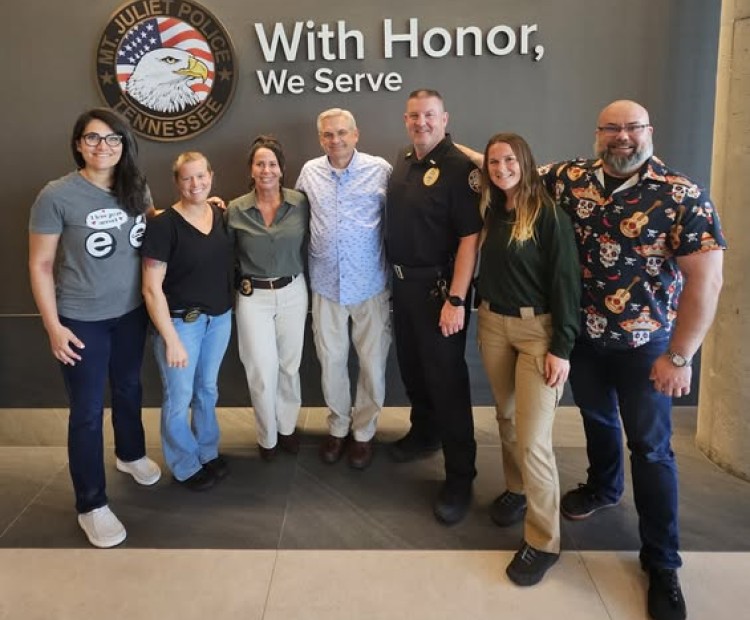 Group of people posing in front of a wall that says With Honor We Serve