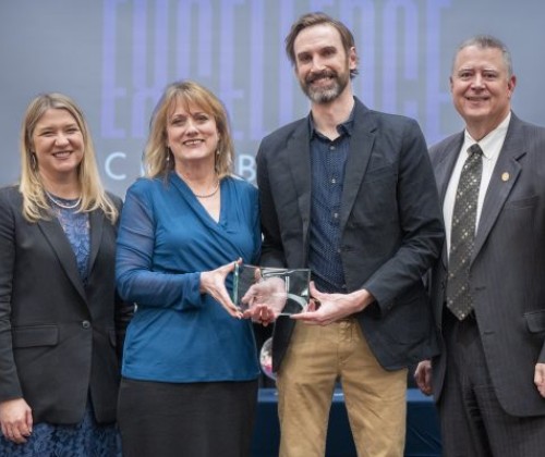 Four people standing with two holding an award 