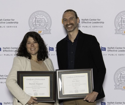 A man and a woman pose with framed certificates