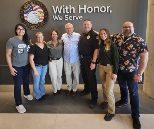 Group of people posing in front of a wall that says With Honor We Serve