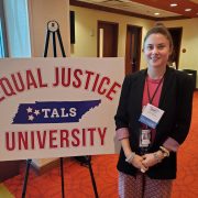Woman in business attire standing next to a sign for the Equal Justice University
