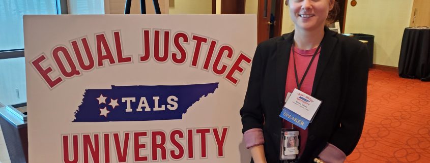 Woman in business attire standing next to a sign for the Equal Justice University