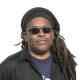 African American man with dreads wearing sunglasses and black shirt over a blue Tshirt