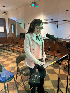 Woman standing in front of a music stand and mike in a recording studio to record a translation.